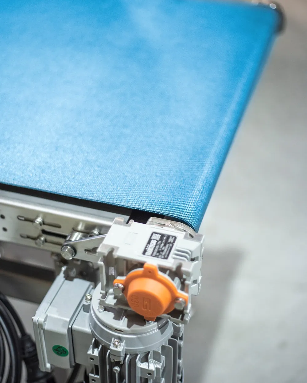 Detalle de un transportador de cinta azul con motorreductor sobre bastidor de acero inoxidable